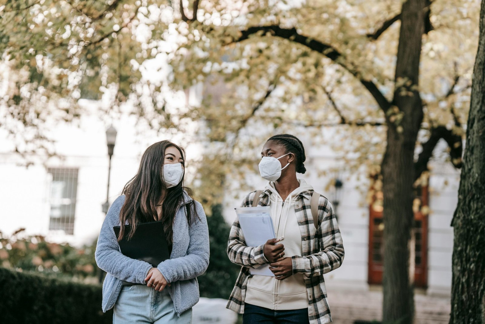 drain-cleaning Low angle of diverse classmates in masks with folders talking about university issues while walking in park together