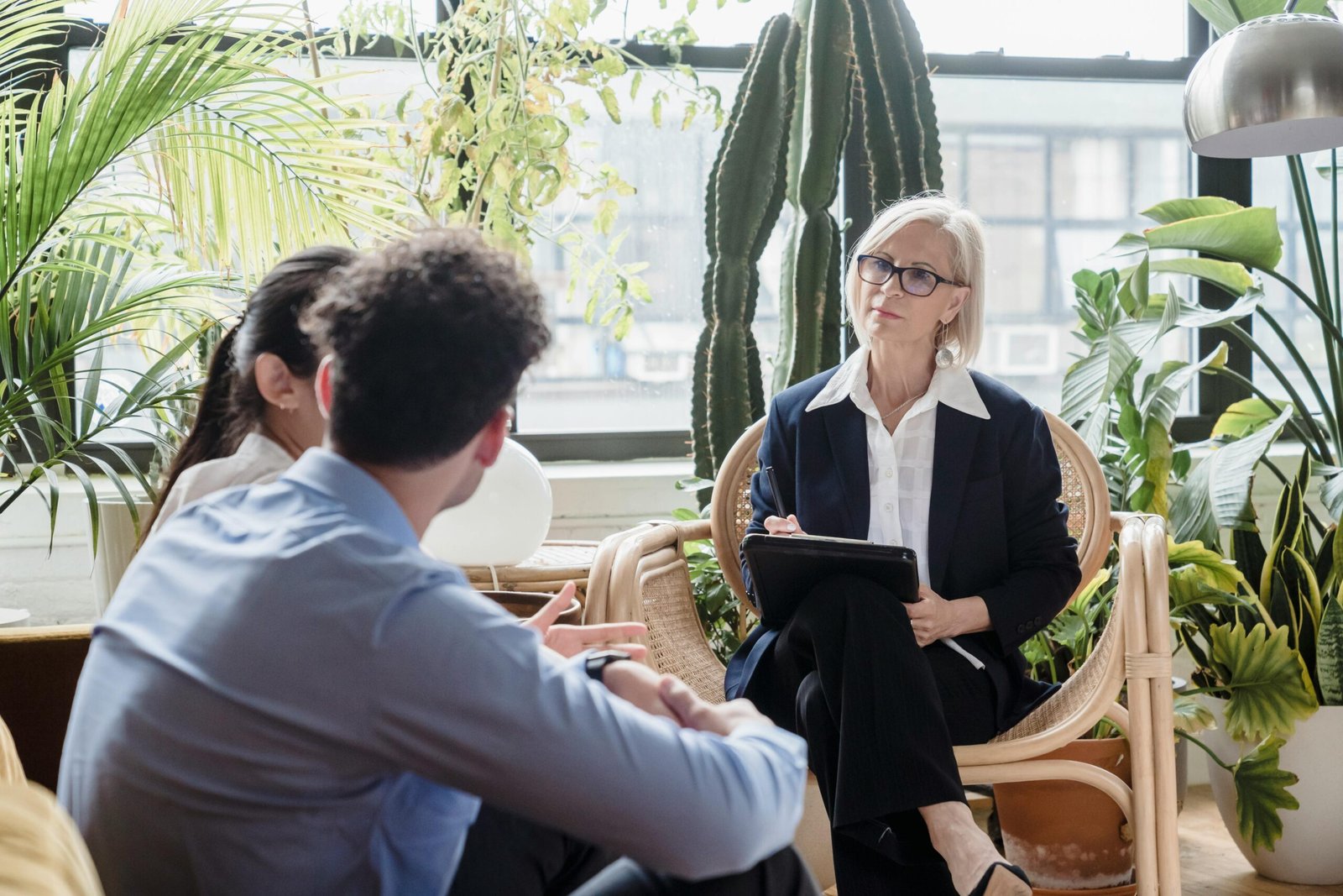 A counselor conducting a therapy session with a couple in a plant-filled room.